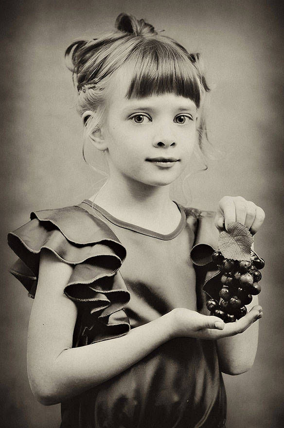 Портрет девочки в детской фотосессии с красивой прической и виноградом в платье с оборками фотограф Борис Никитин 
